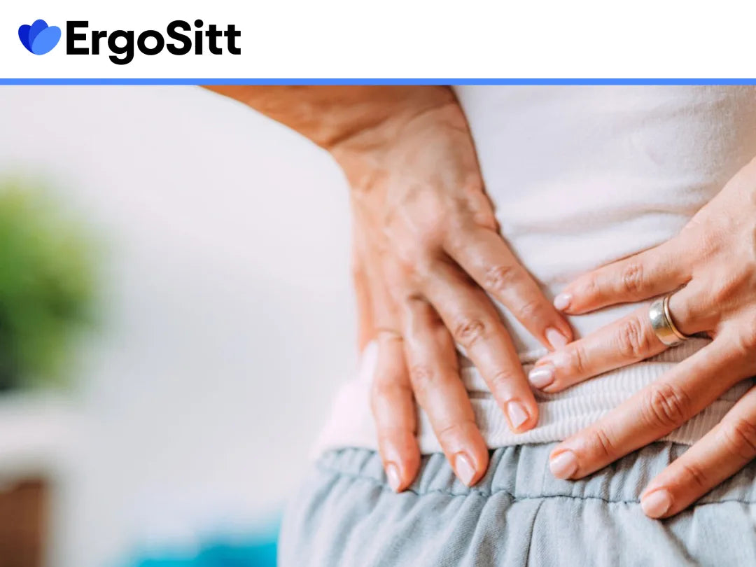 Äldre kvinna med svanskotesmärta som sitter i fåtölj hemma och visar tydlig smärta i nedre ryggen