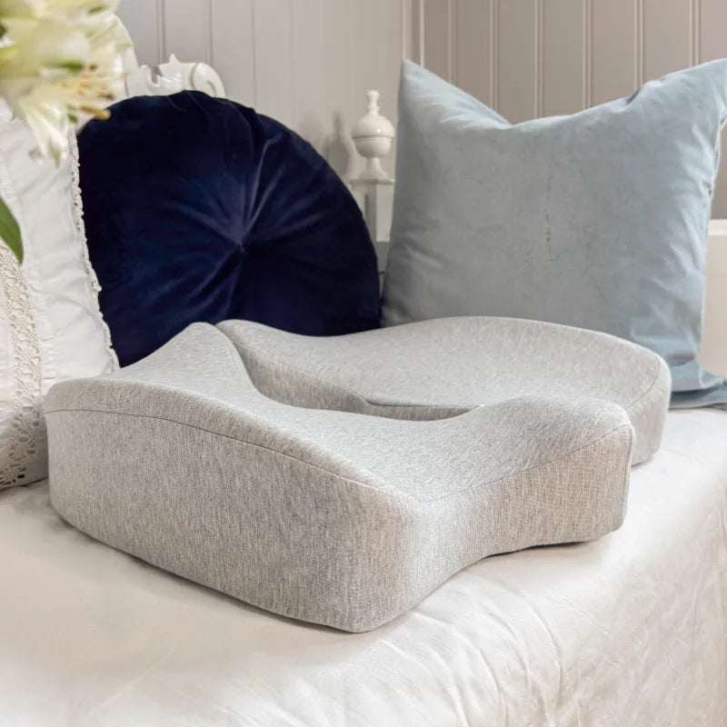 Tryckavlastande ergonomisk sittkudde i grått minnesskum placerad på ljus soffa med blåa kuddar i bakgrunden