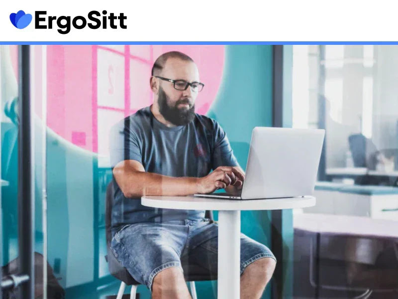 Man sitter vid ett skrivbord med laptop i modern kontorsmiljö – illustration av ergonomiska utmaningar vid stillasittande arbete.