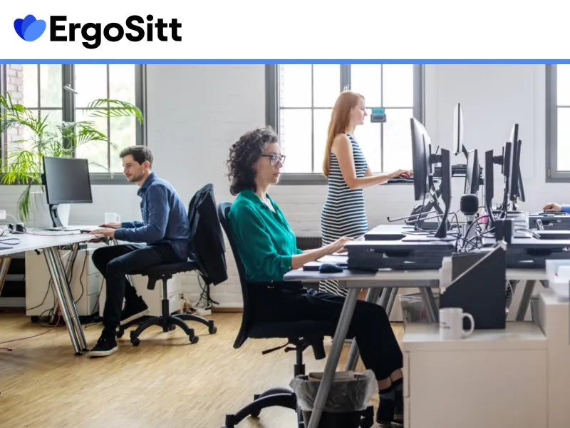 Personer arbetar i ett modernt kontor med sitt- och ståbord – exempel på ergonomisk arbetsmiljö för att förebygga ryggont.