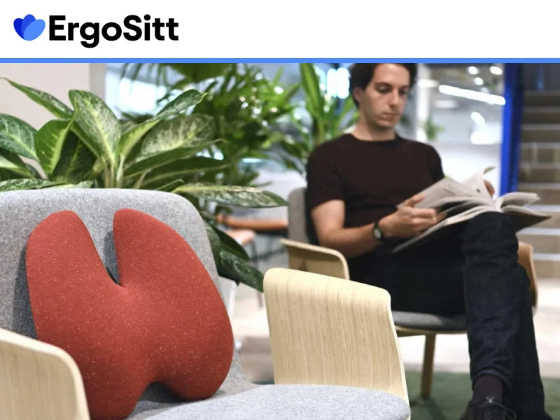 Man i loungeområde med röd ErgoStöd på stol – en ergonomisk ländryggskudde för ryggstöd och avlastning i vardagen.