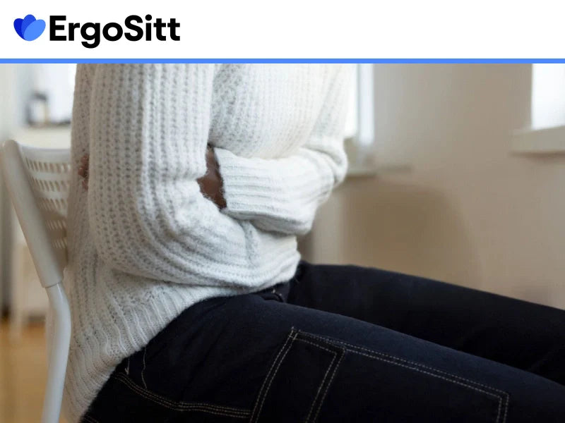 Kvinna med smärta i kroppen sitter försiktigt på stol – visar hur trycksår kan lindras vid långvarigt sittande.