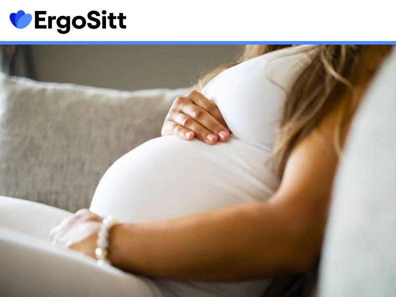 Gravid kvinna sitter i soffa med handen på magen – ergonomiska tips för att lindra smärta vid sittande under graviditet