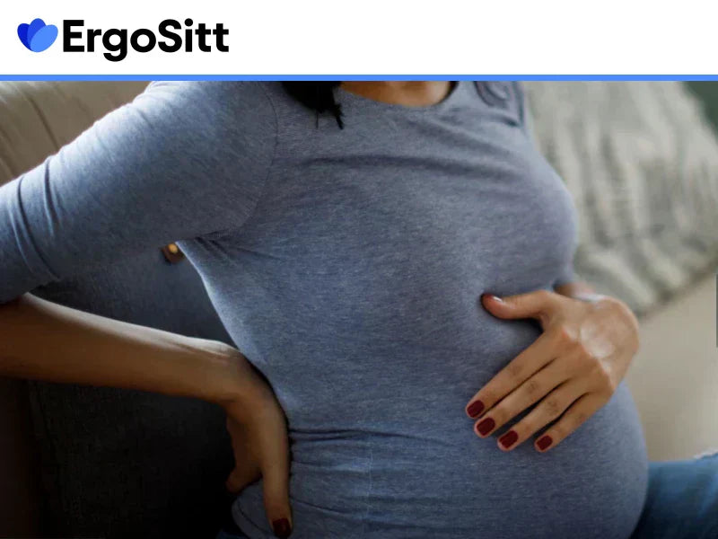 Gravid kvinna sitter med handen på svanken och visar tydliga tecken på ryggsmärta i sittande position