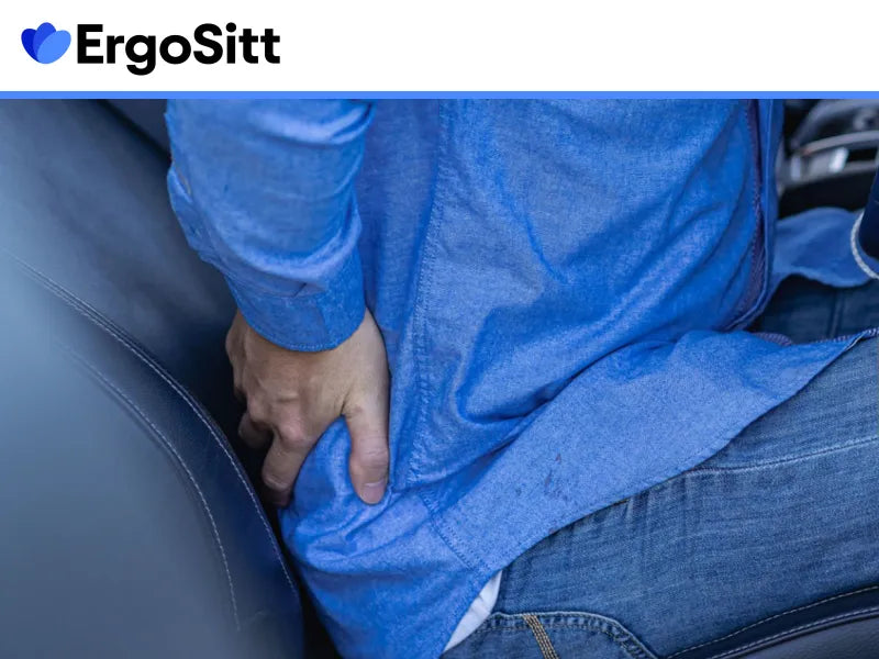 Man sitter i bil med handen mot ländryggen – upplever smärta som kan lindras med ergonomisk sittdyna för bilstol.