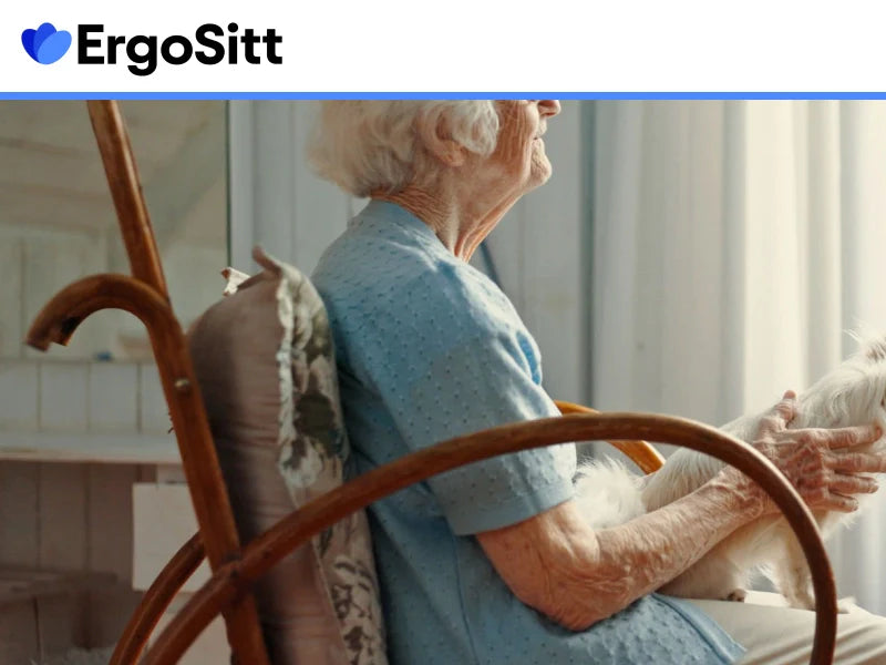 Äldre kvinna sitter bekvämt med stödjande sittkudde i hemmet och håller en liten hund i famnen