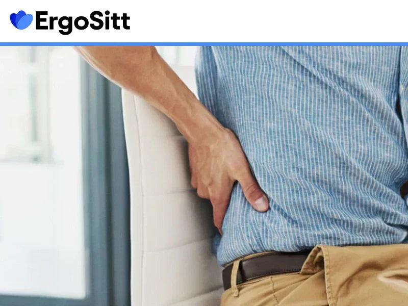 Man med blå skjorta håller sig för ländryggen medan han sitter på en kontorsstol, tyder på stelhet eller smärta från långvarigt stillasittande