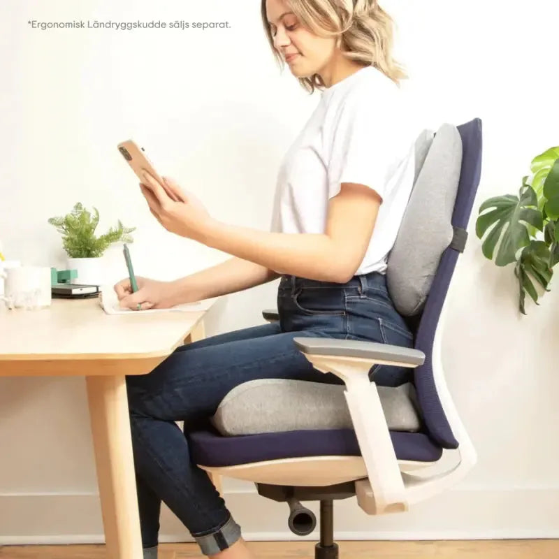 Kvinna sitter bekvämt på en ergonomisk sittkudde vid ett skrivbord, perfekt för kontorsstolar.