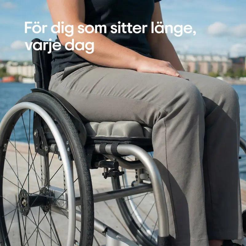 Person sitter på ErgoCell sittkudde i rullstol vid vattnet en solig dag — tryckavlastande sittkudde för dig som sitter länge varje dag